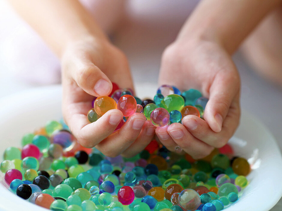 Kinderhände greifen bunte Wasserperlen aus einer Schale